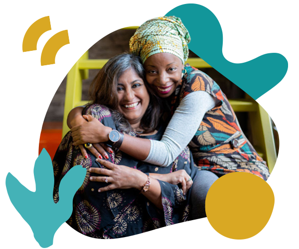 Two women embrace and look at the camera while in a Reimagining Collaboration training